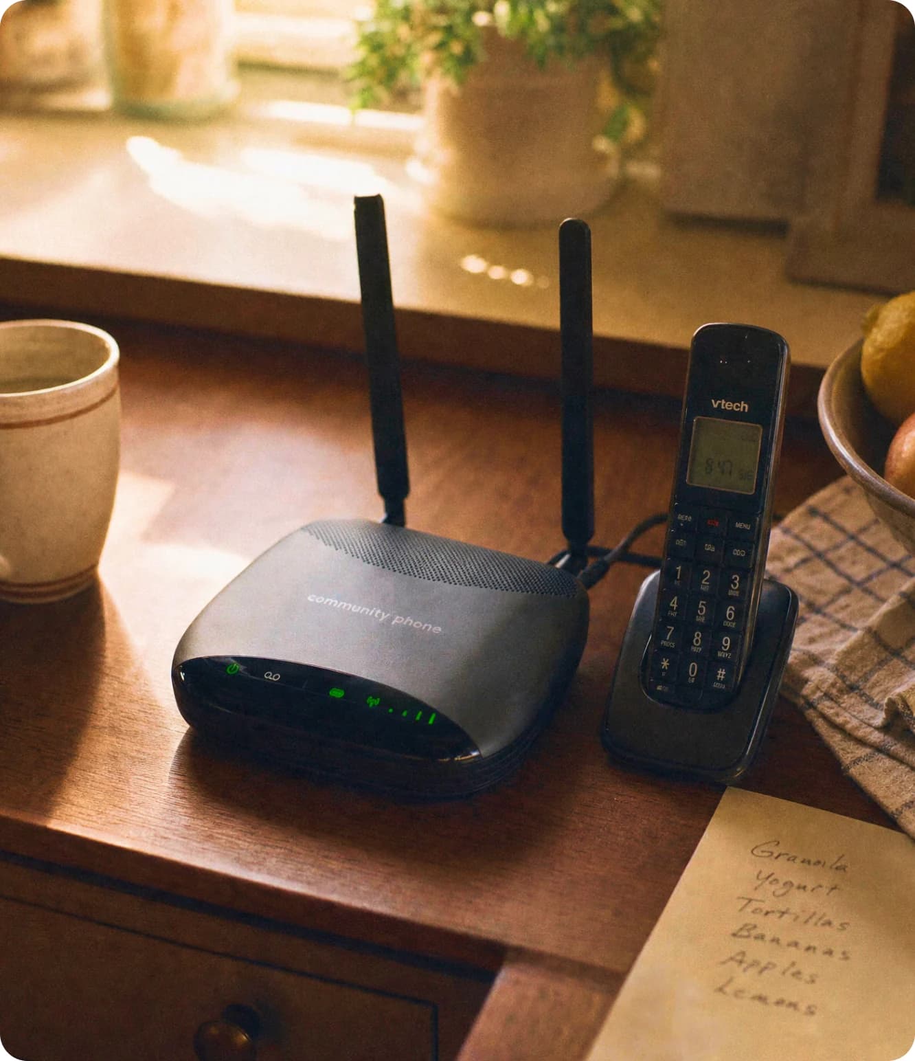 Community Phone Base and cordless handset on a kitchen table next to a handwritten grocery list